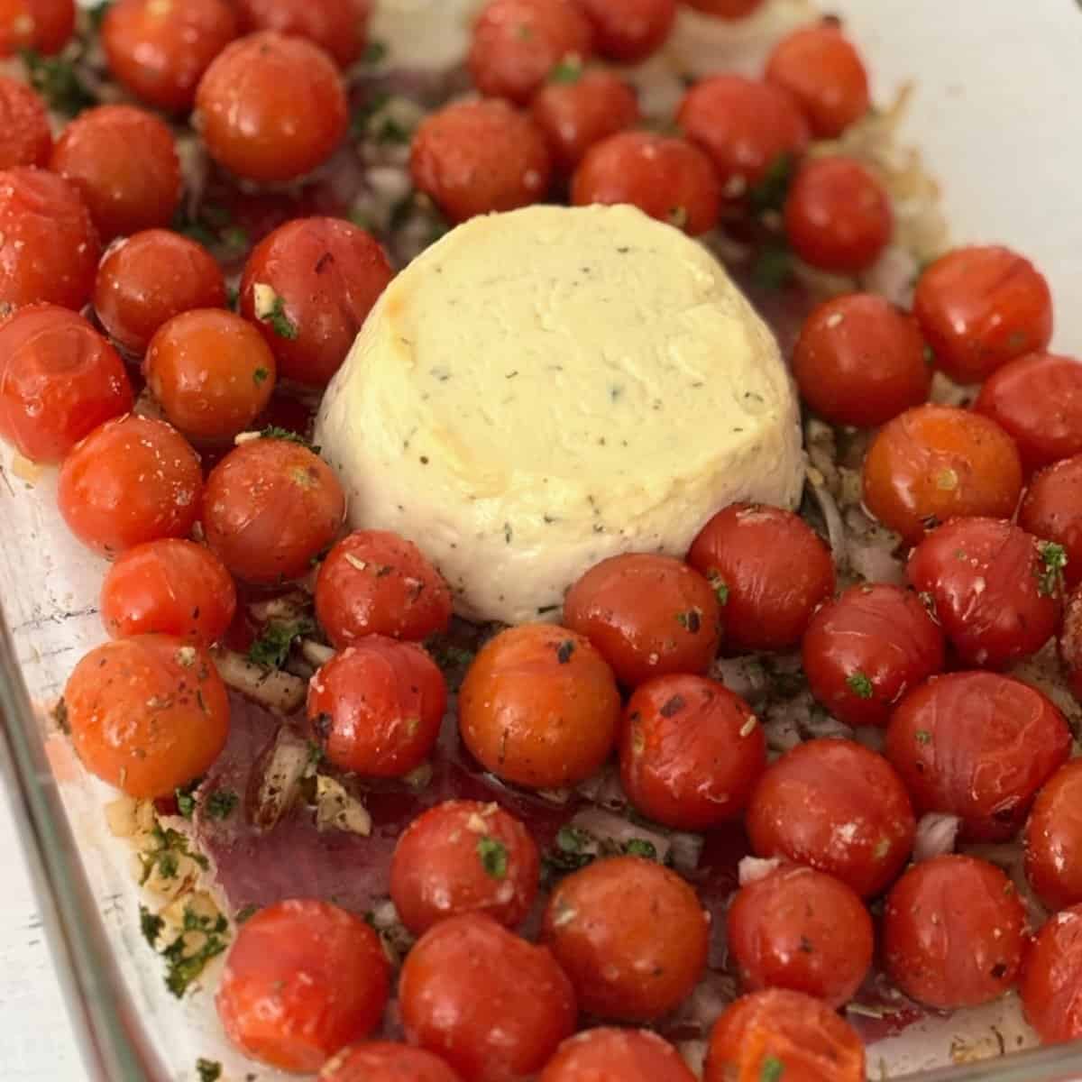 A block of boursin cheese in a casserole dish surrounded by red cherry tomatoes. 