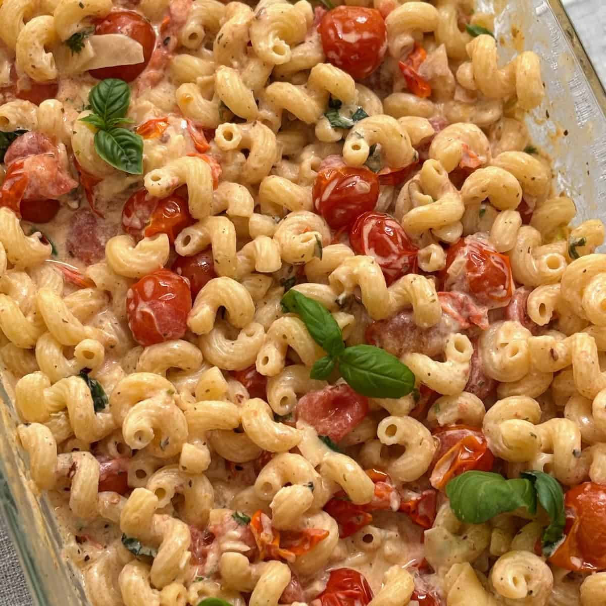 A casserole dish full of pasta mixed with boursin cheese, veggies and seasoning. 