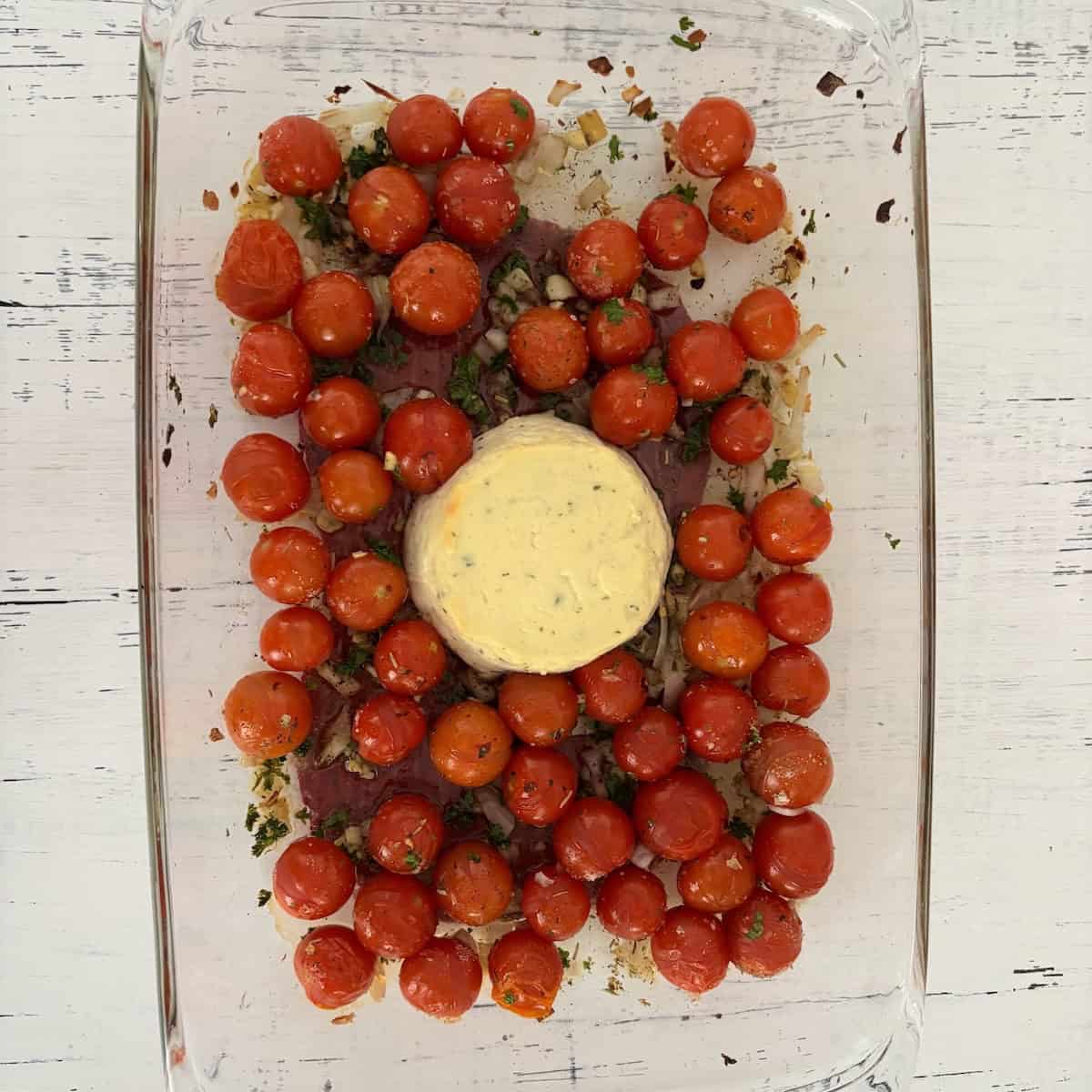 Cherry tomatoes, seasoning, veggies and boursin cheese in a casserole dish after baking in the oven. 
