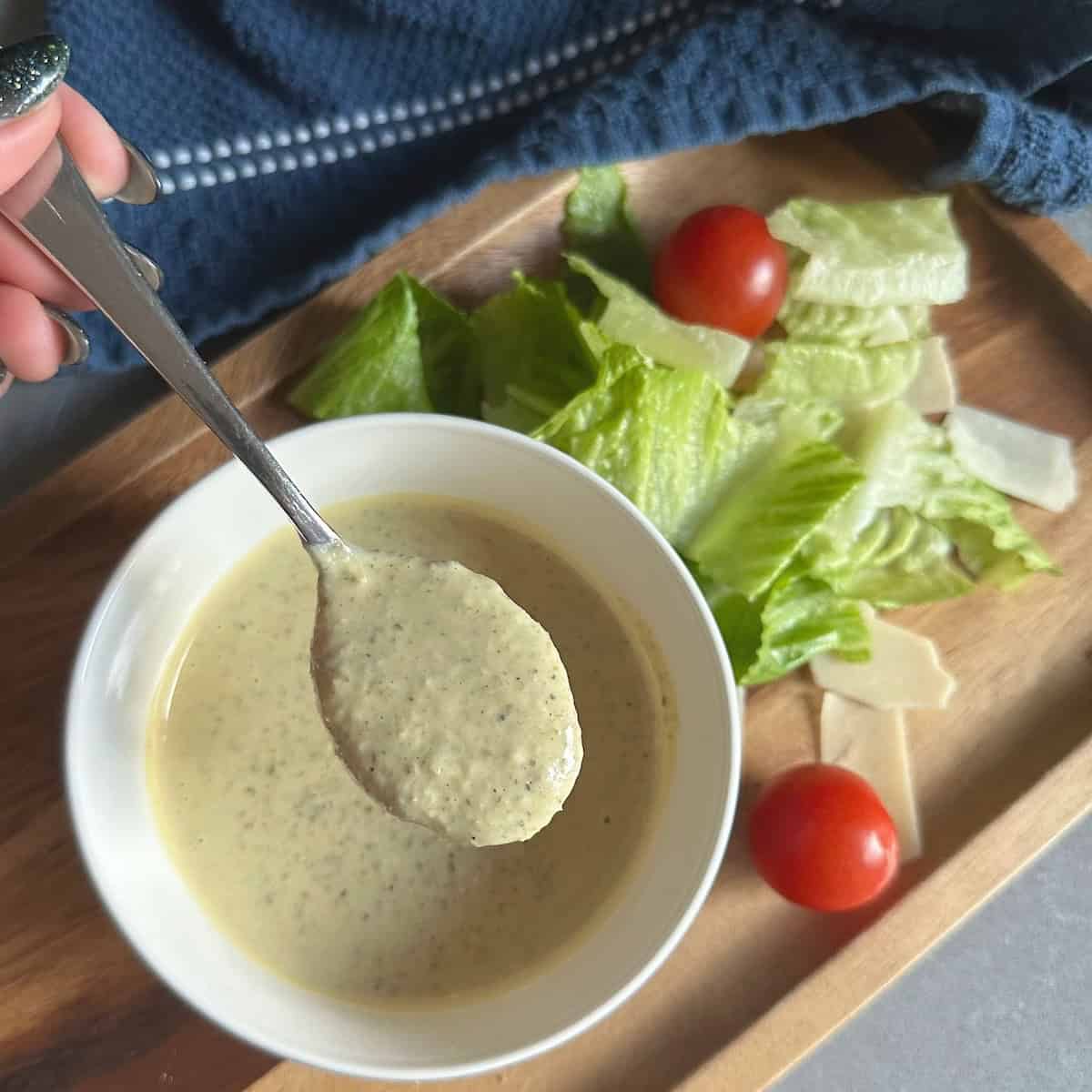 spoonful of Caesar dressing hovering above bowl, with blue napkin and salad below