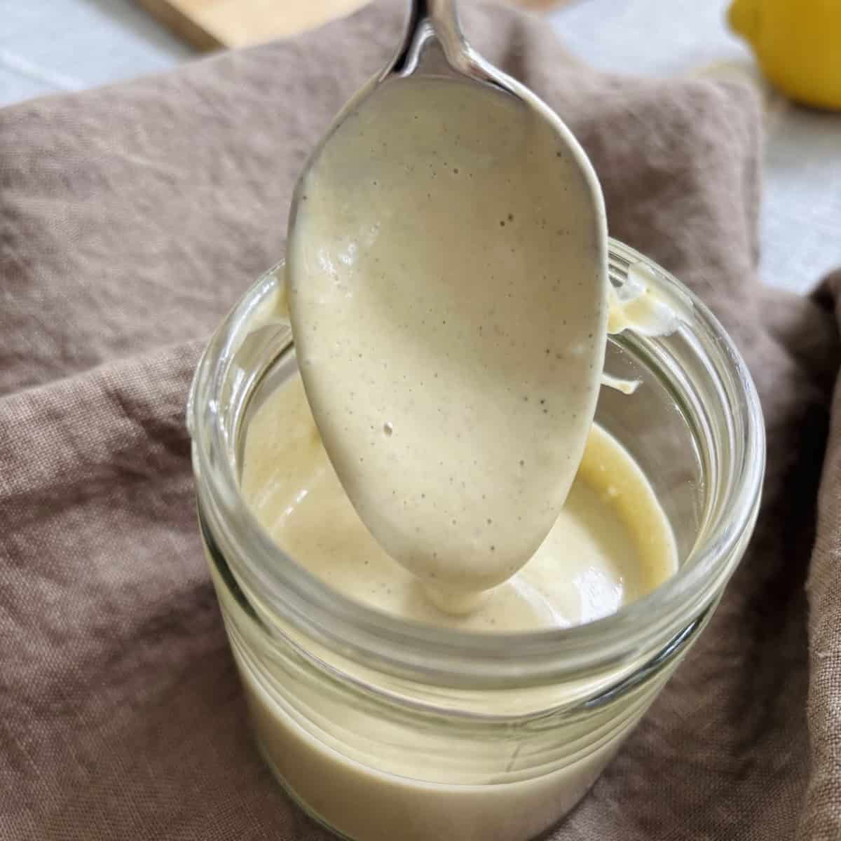 Caesar dressing dropping off a spoon into a mason jar full of the rest of the dressing.