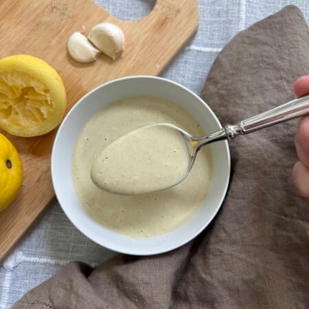 A spoon full of caesar dressing held over a white bowl full of the dressing.
