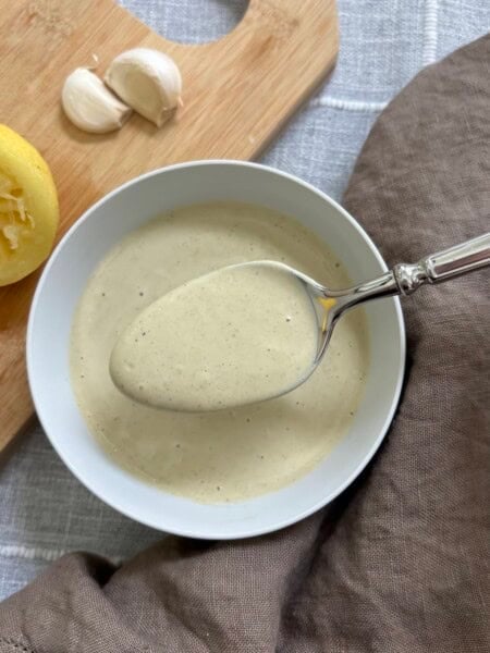 A spoon full of caesar dressing held over a white bowl full of the dressing.