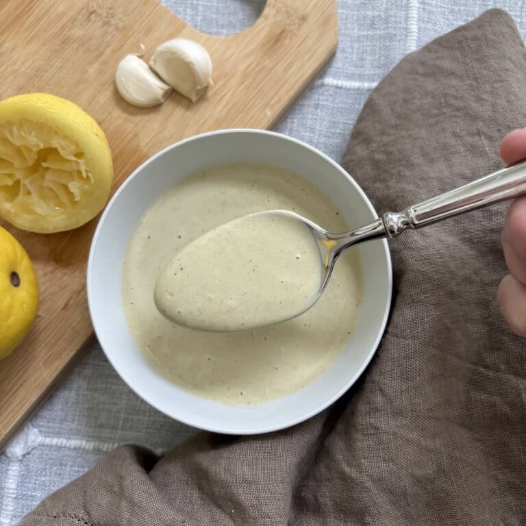 A spoon full of caesar dressing held over a white bowl full of the dressing.