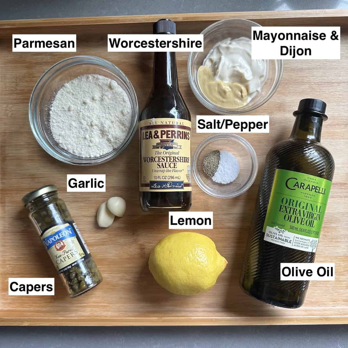 Ingredients for caesar dressing with capers on a white table.