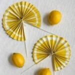 Two lemon fan crafts on a white table surrounded by 3 lemons.