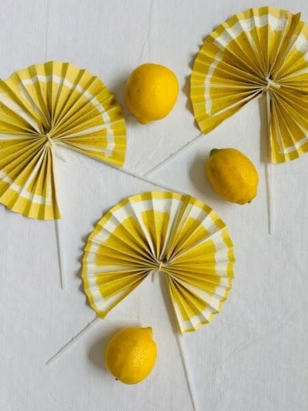 Three yellow fans decorated and painted to look like lemons surrounded by three real lemons.