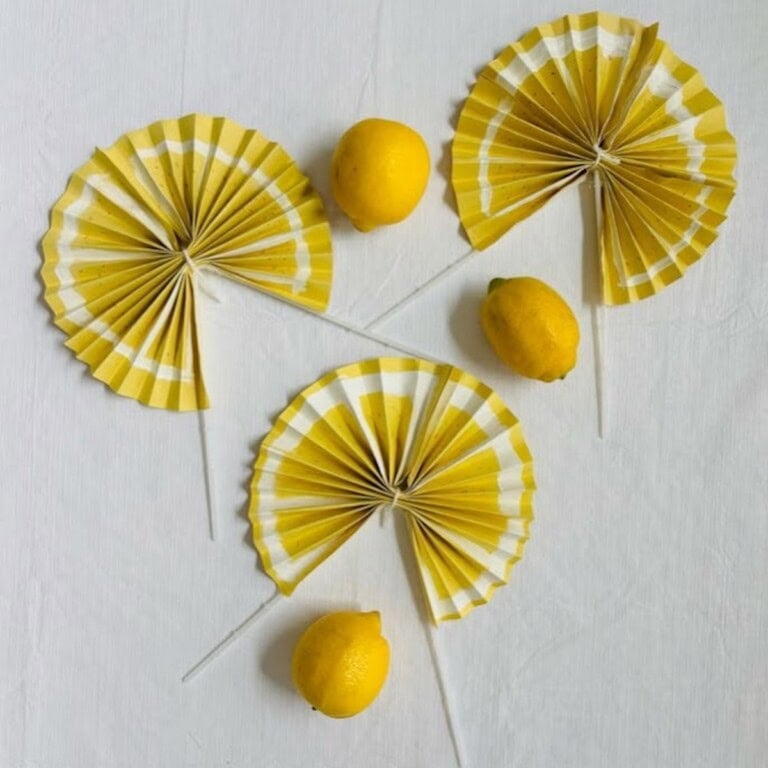 Three yellow fans decorated and painted to look like lemons surrounded by three real lemons.