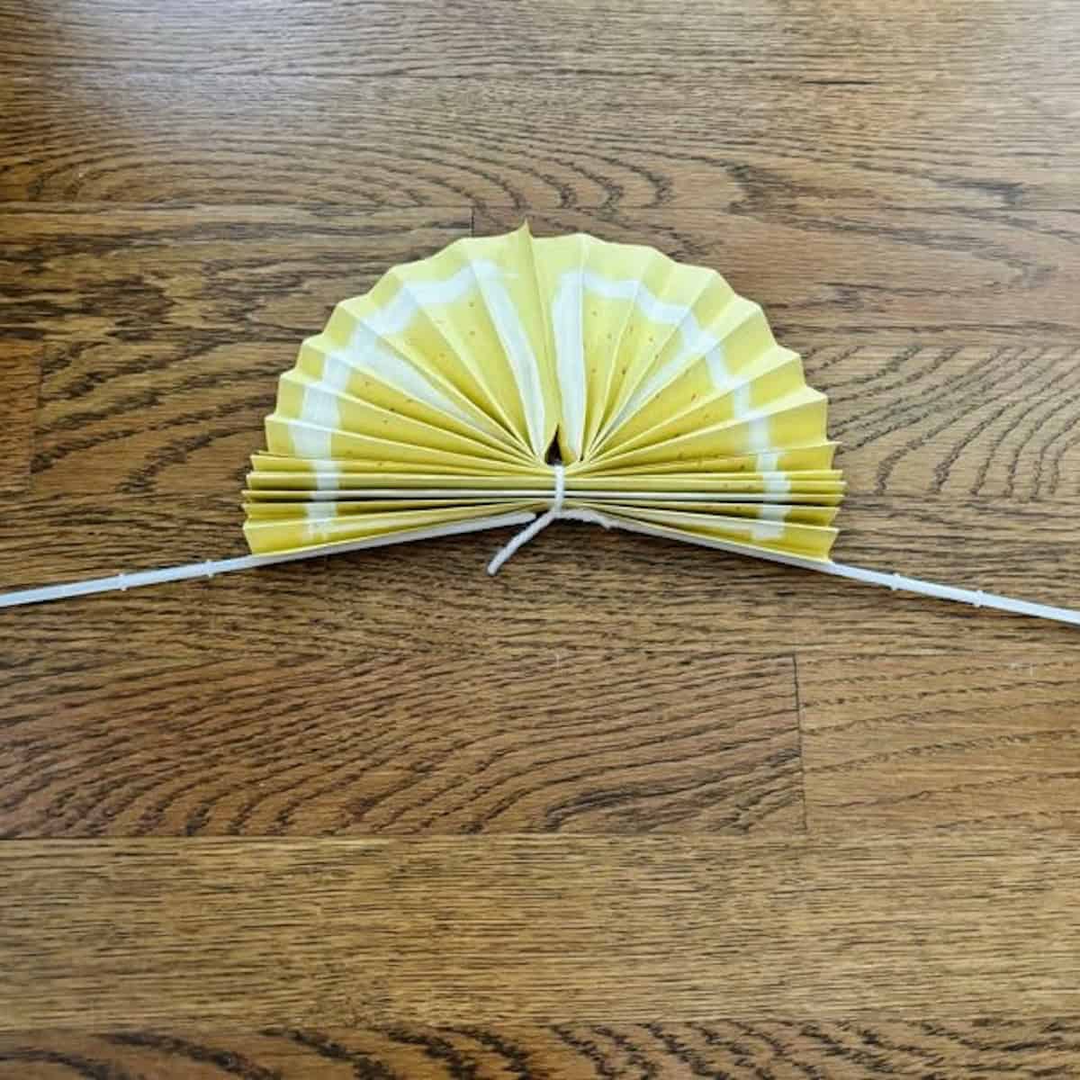 A yellow lemon fan with two sticks glued to bottom to form its handles.