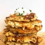 A stack of cheesy potato pancakes topped with a dollop of sour cream and chives.