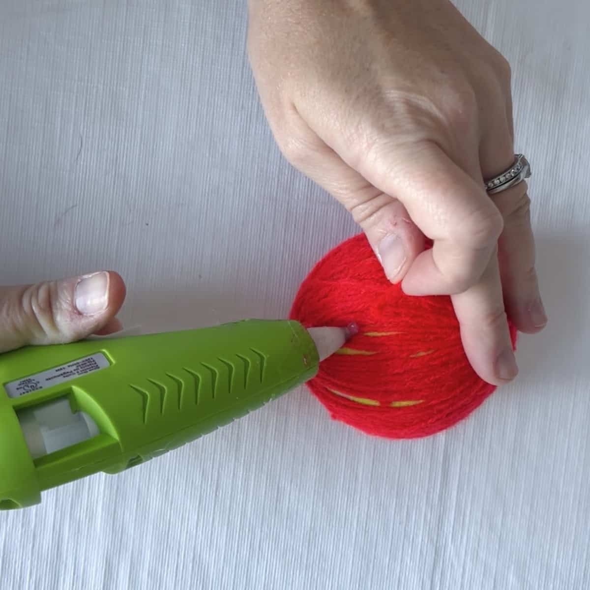 Gluing the end of yarn to a wrapped tennis ball for an apple craft.