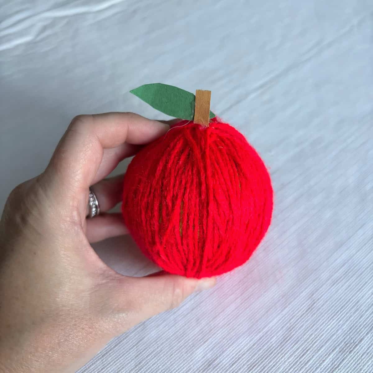 A tennis ball made to look like a red apple by wrapping with red yarn and gluing on a paper stem.