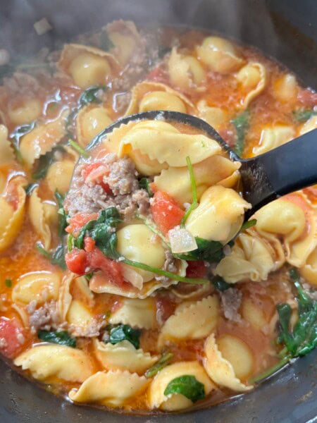 Closeup of sausage tortellini soup in ladle.