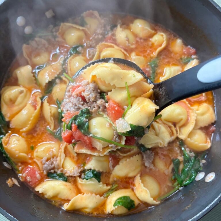Closeup of sausage tortellini soup in ladle.