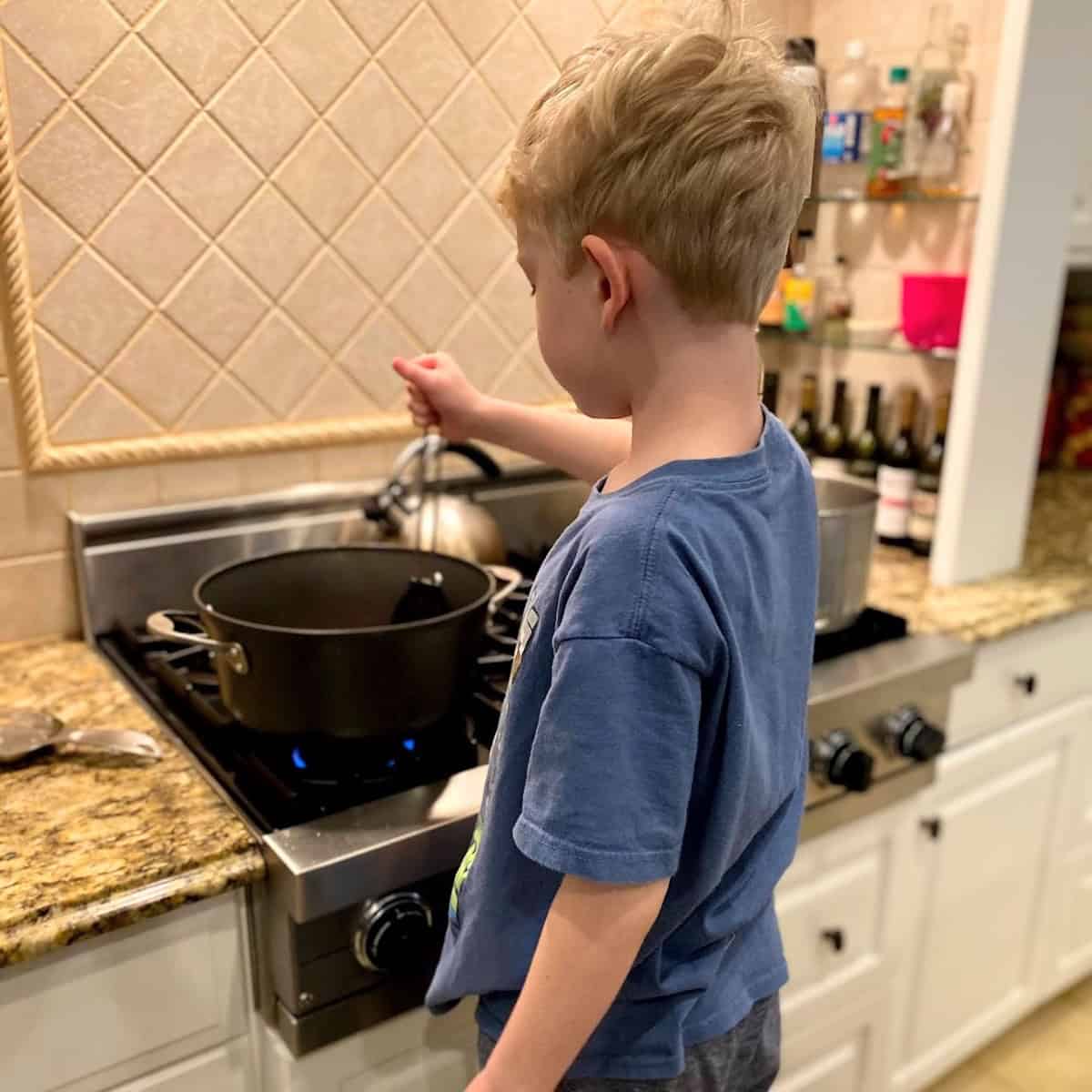 A boy stirring something over the stove in a large pot.