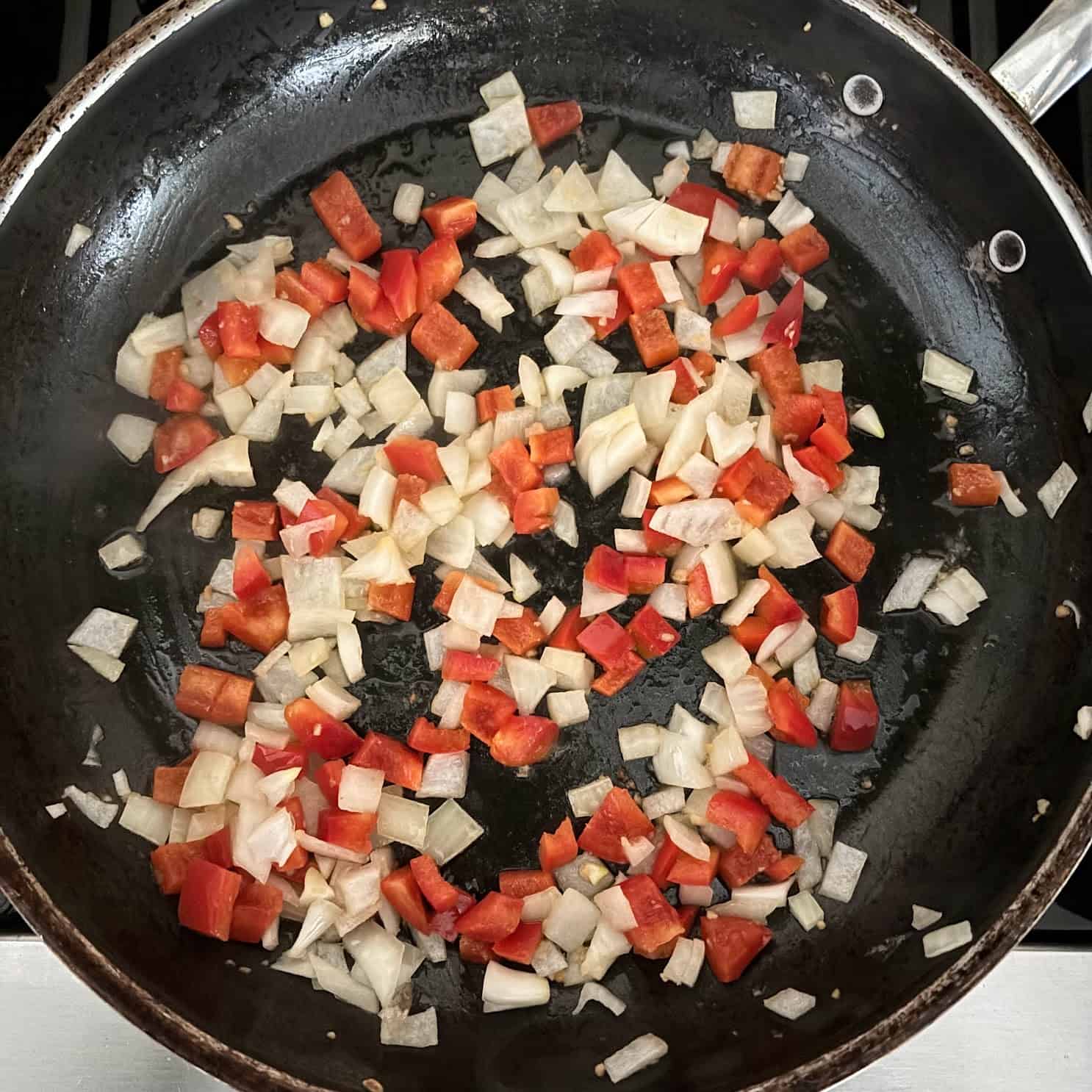 Chopped onion, red pepper and garlic cooking in a black pan for turkey enchilada skillet.