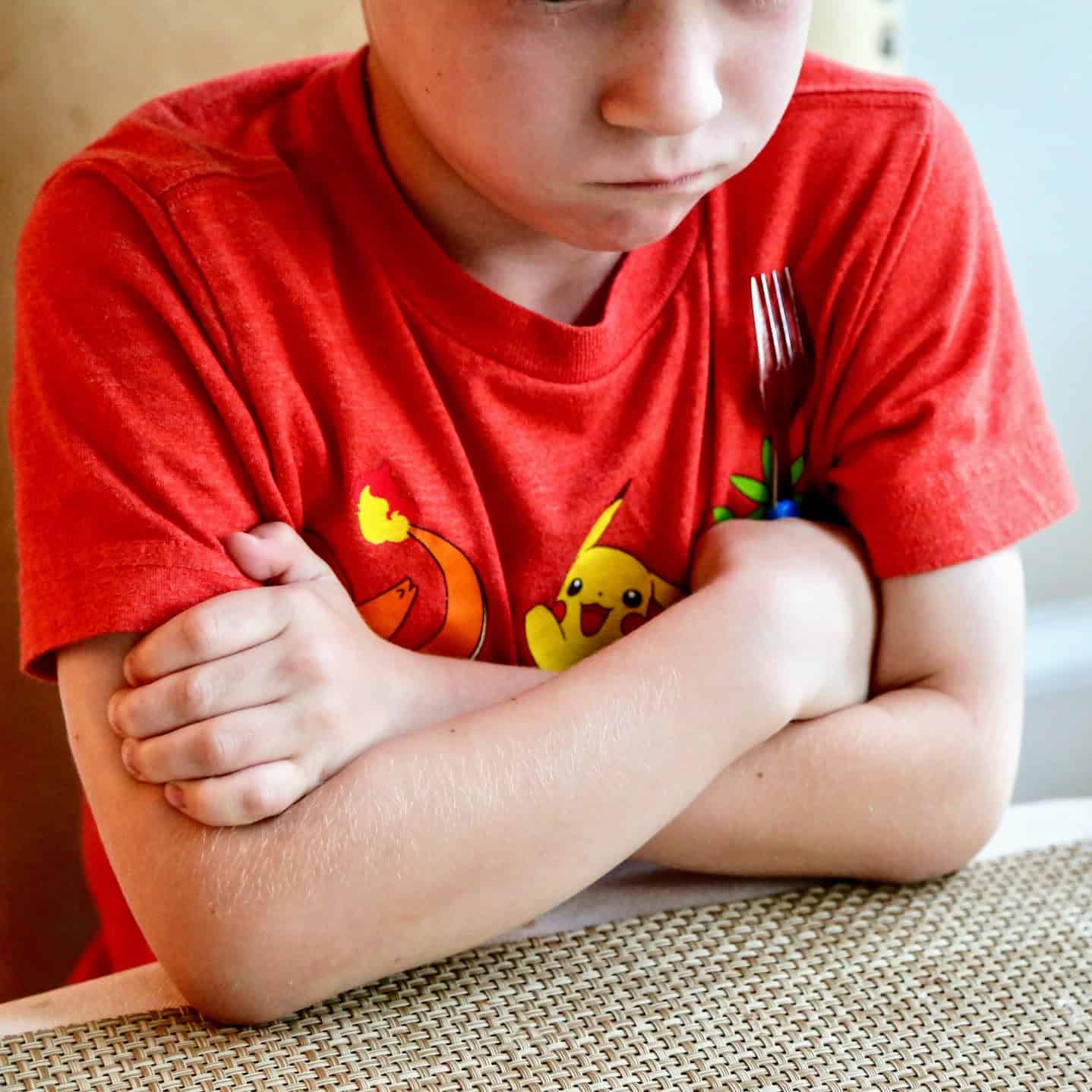 Child sitting at dinner table looking upset and holding a fork.
