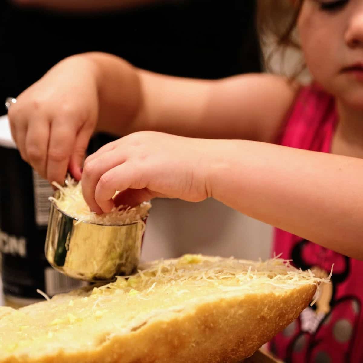 Little girl sprinkling parmesan cheese on bread