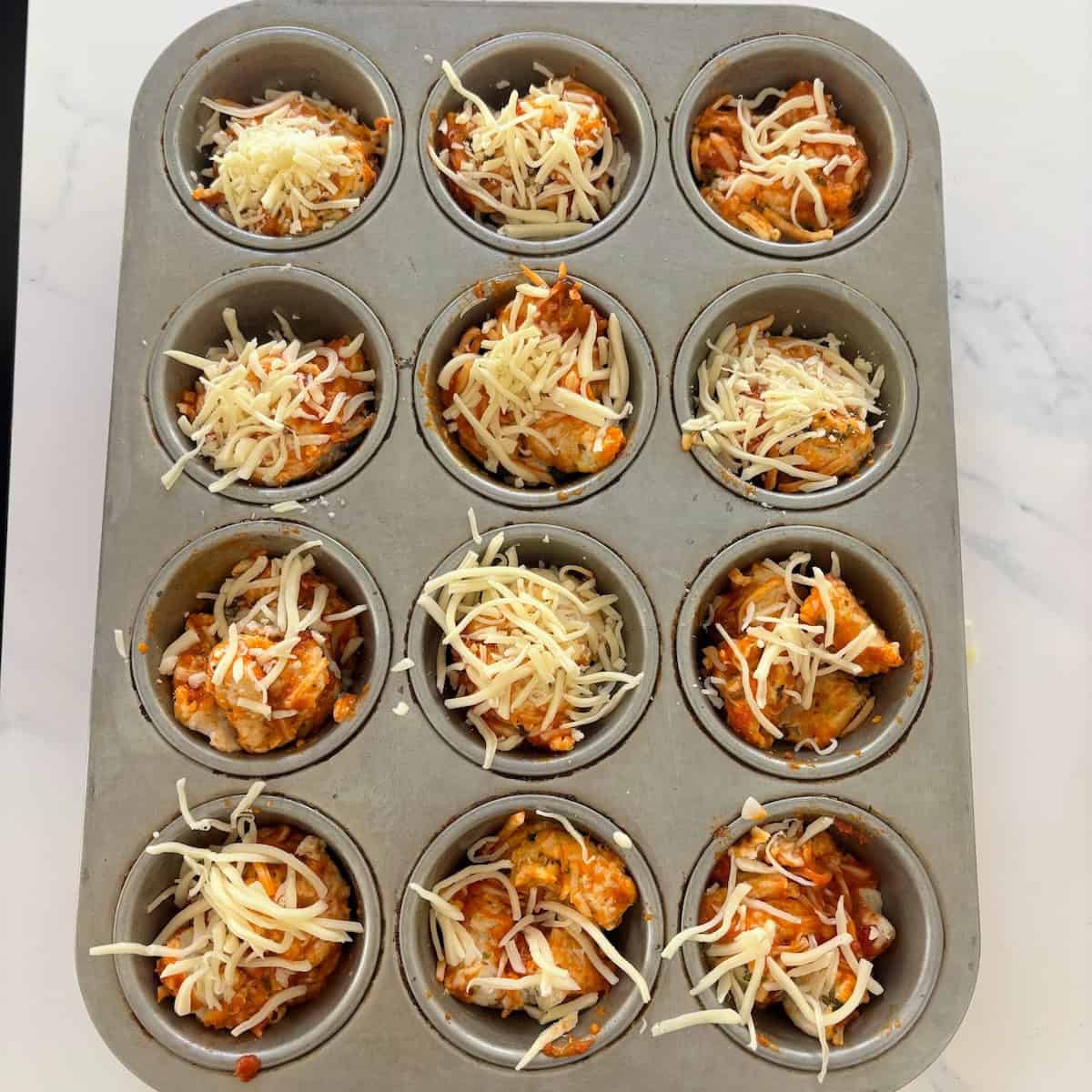 Mini meatloaf muffins topped with shredded cheese in a muffin tin.