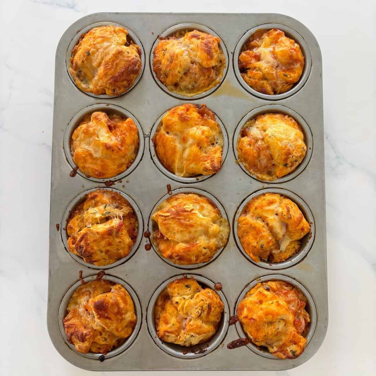 Cooked pizza muffins with biscuits in muffin tin.