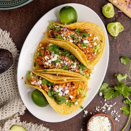 Three chicken tinga tacos on a white plate with limes on the side, a quick dinner without a stove or oven.