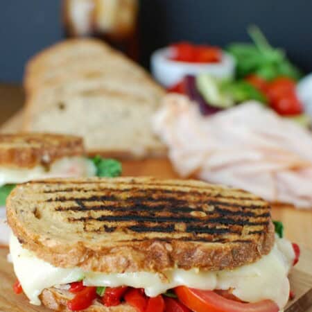 A pressed Mediterranean turkey and hummus panini, sliced and served on a wooden cutting board