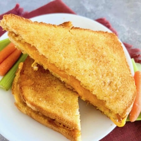 A golden grilled cheese sandwich served with a side of fresh veggies on a white plate