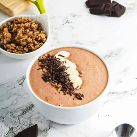 Chocolate peanut butter smoothie bowl in a white bowl with a side of granola.
